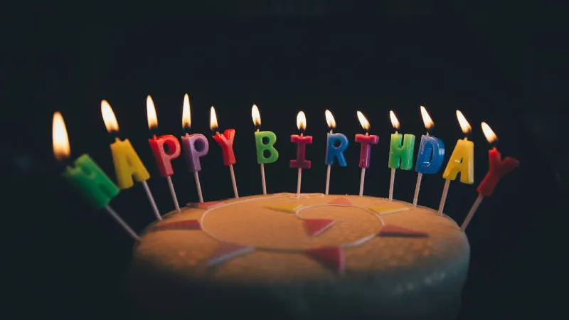 Ein Kuchen mit brennenden Kerzen darauf. Die Kerzen bilden den Schriftzug "Happy Birthday".