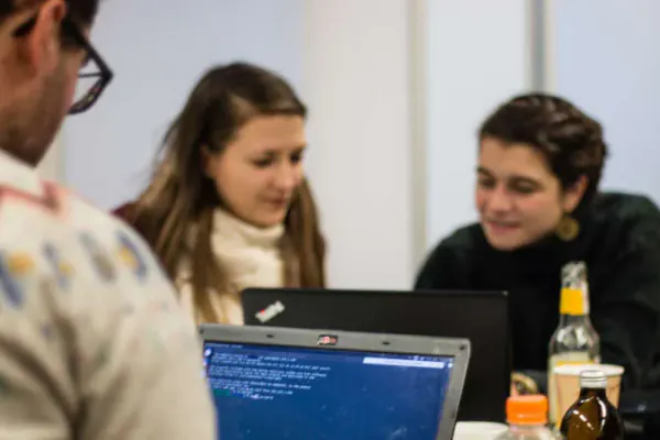 Man sieht mehrere Personen, die zusammensitzen und gemeinsam an zwei Laptops arbeiten.